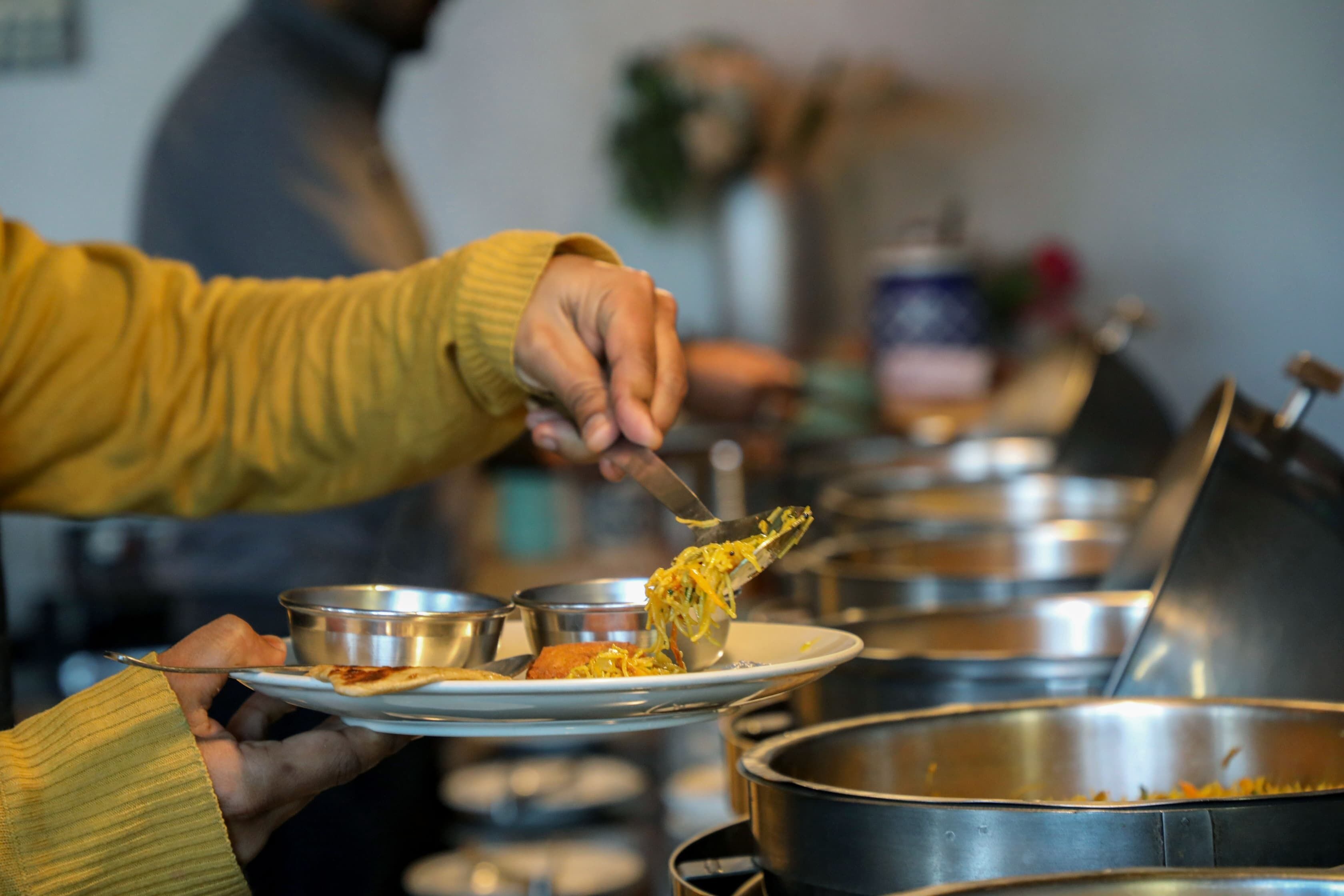 Mesa de buffet con varios recipientes metálicos y una persona sirviendo comida.