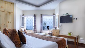 Une chambre d’hôtel moderne dotée d’un grand lit, d’un bureau, d’un téléviseur fixé au mur et de grandes fenêtres avec des rideaux.
