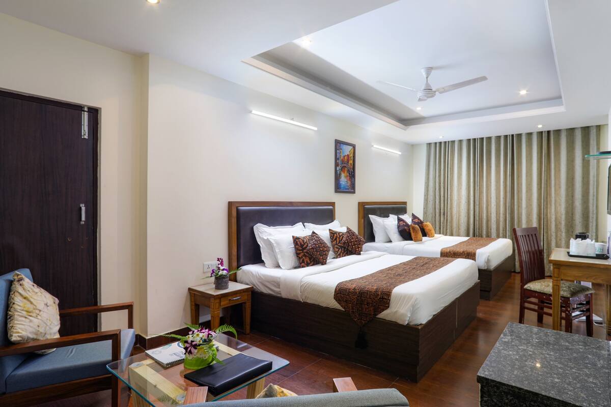 A hotel room with two beds, a desk, a chair, a small table, and a ceiling fan.