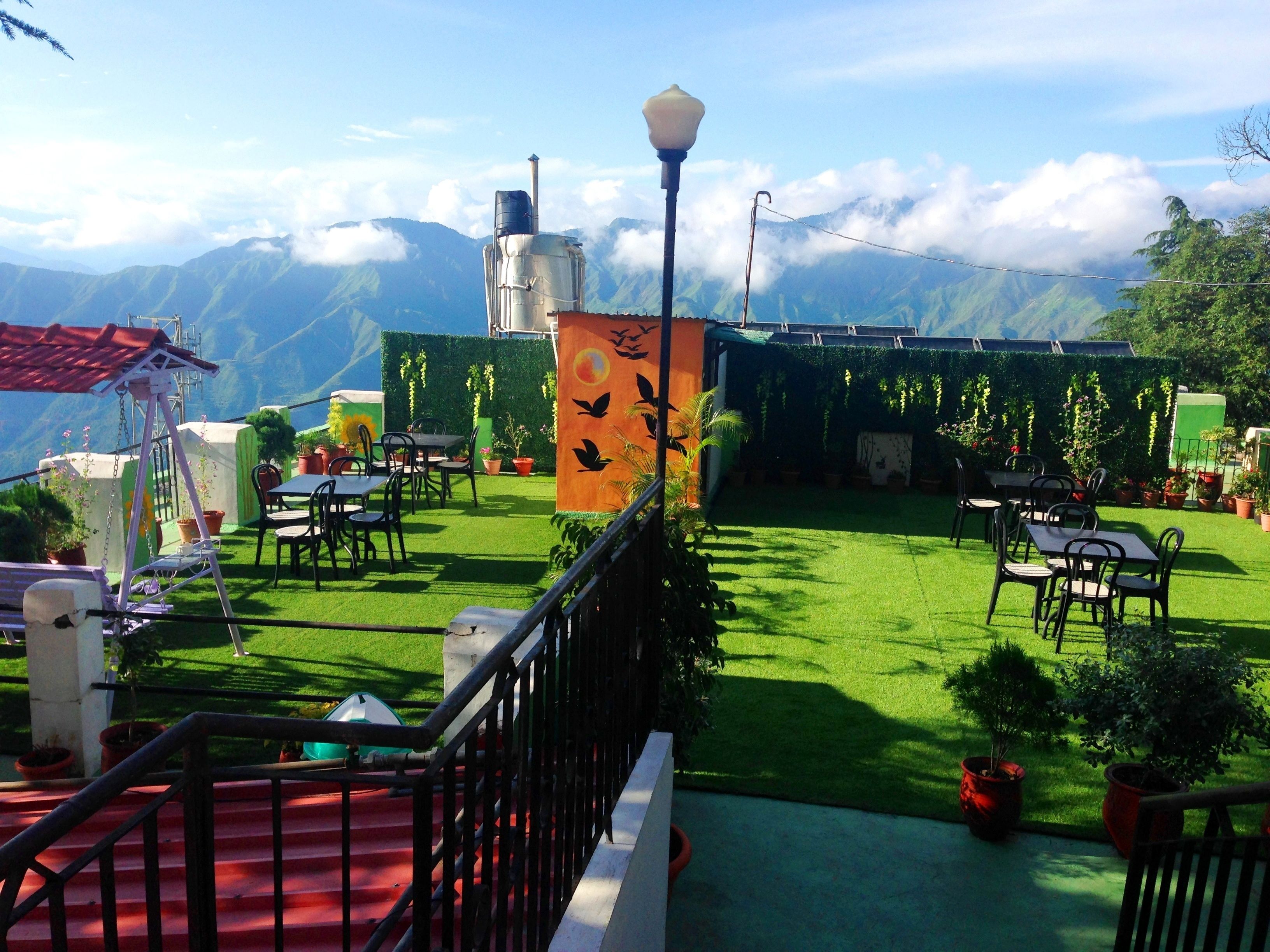Une terrasse agrémentée de tables et de chaises, entourée de plantes en pot et offrant une vue sur les montagnes.