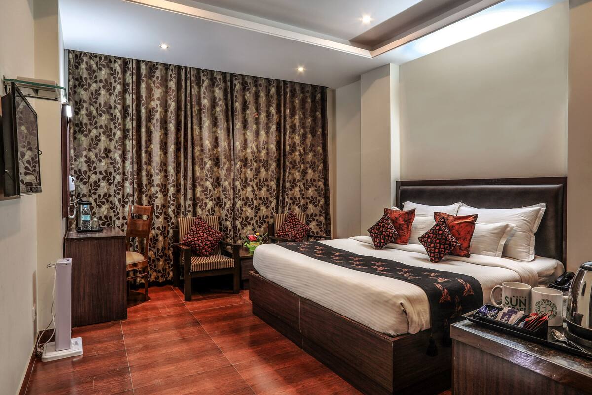 A hotel room with a large bed, a desk with a telephone, a chair, and a coffee maker on the side.