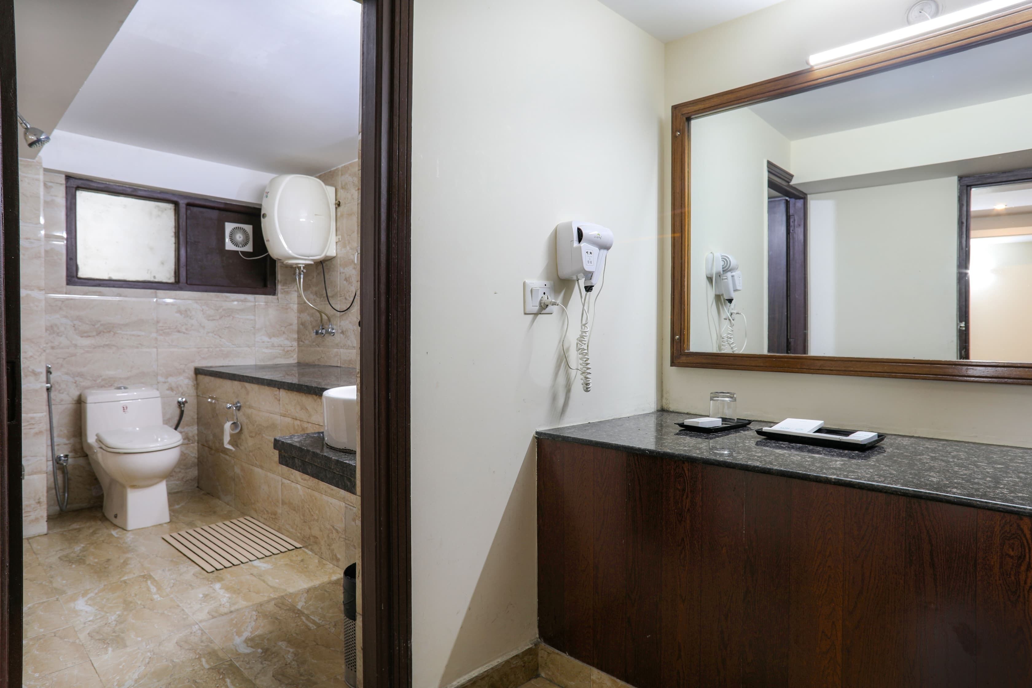 A bathroom with a toilet, sink, mirror, and a hairdryer on the counter.