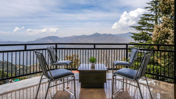 Un balcon avec une table et quatre chaises, donnant sur un paysage montagneux.