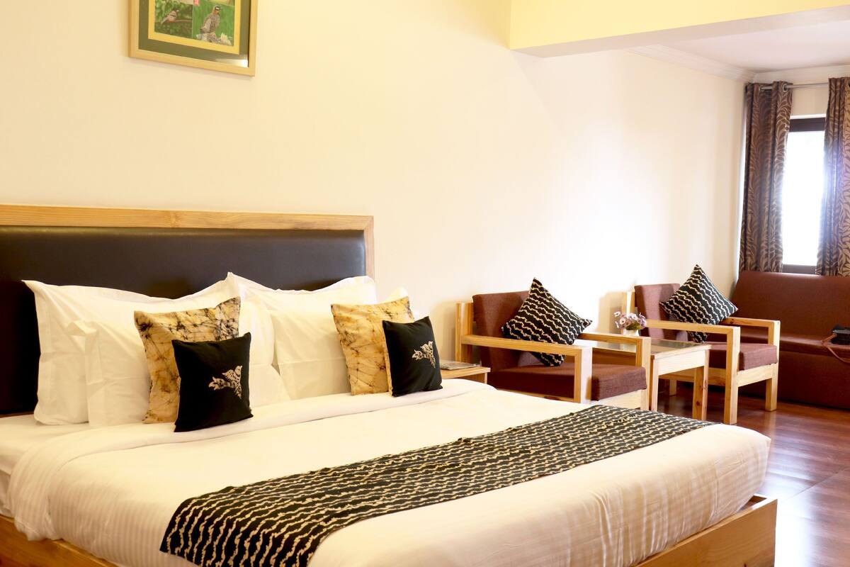 A neatly arranged hotel room with a large bed, a wooden headboard, a small table, two chairs, and a sofa.