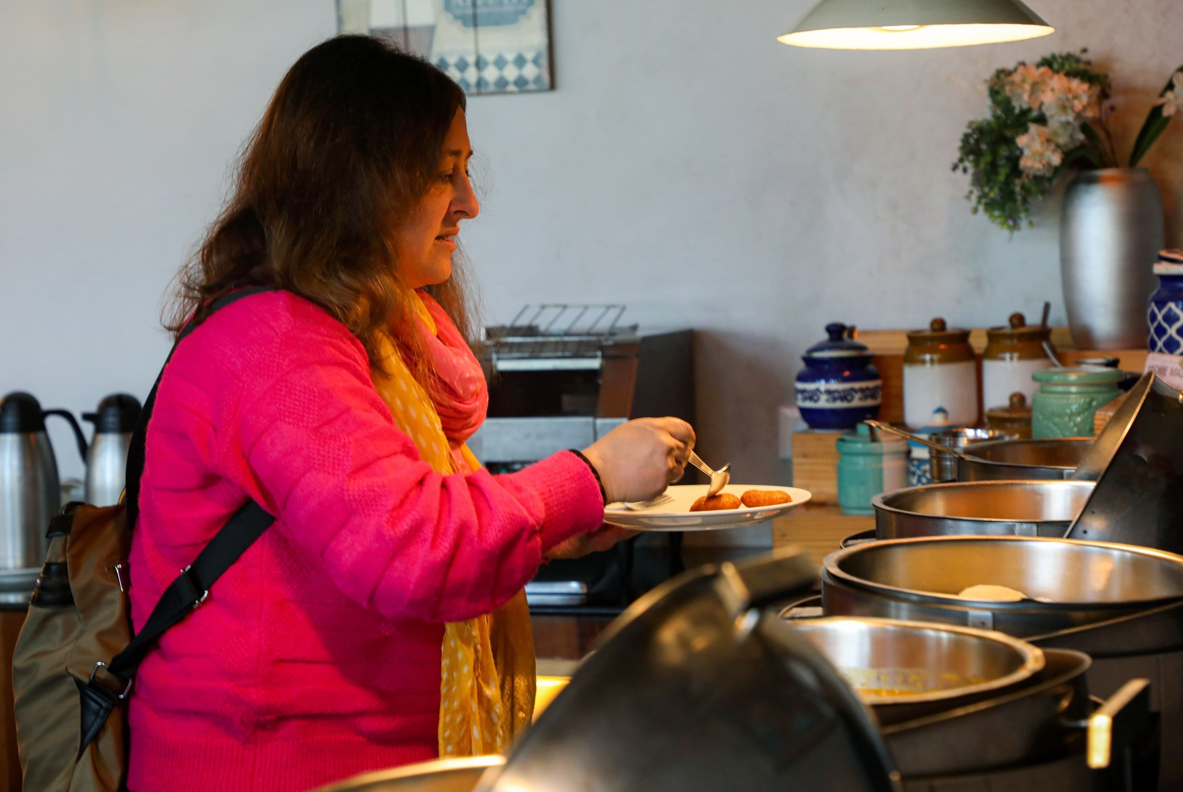 Une personne portant une veste rose se sert au buffet, qui propose divers plats et ustensiles.
