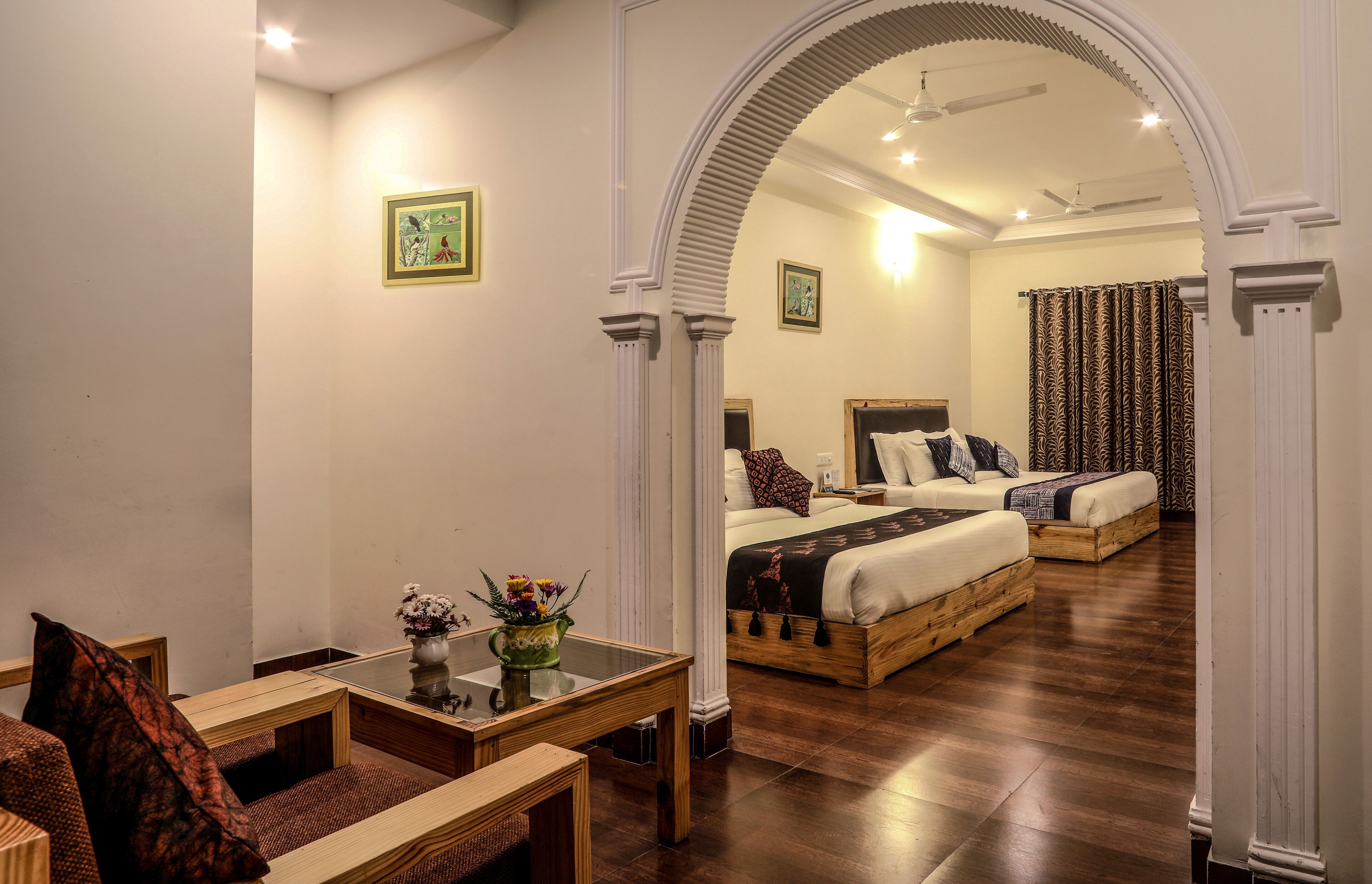 A hotel room with a wooden floor, a bed with a headboard, a bedside table with a vase of flowers, and a chair.