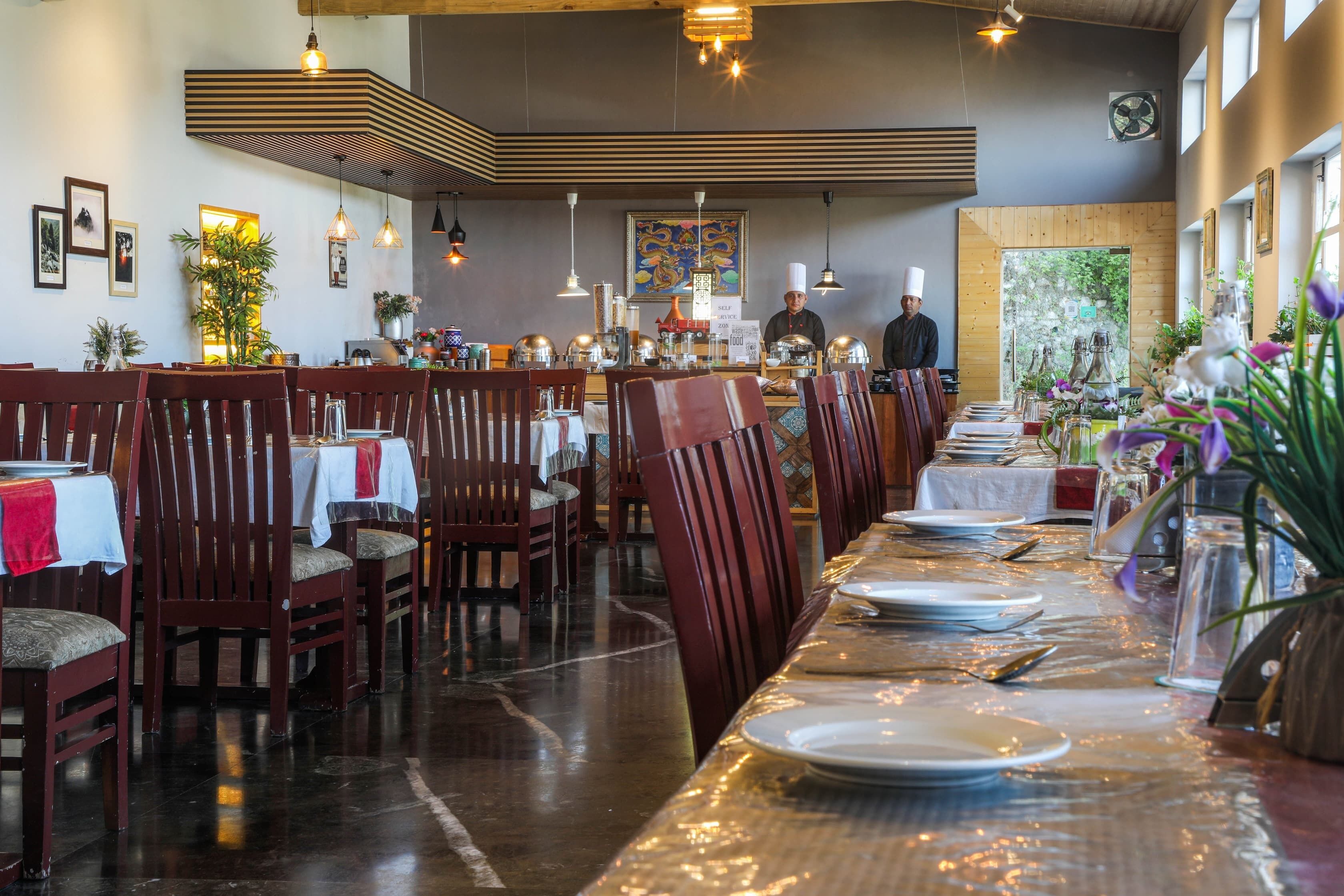 Een restaurant met houten tafels en stoelen, een lange toonbank en een kok in uniform.