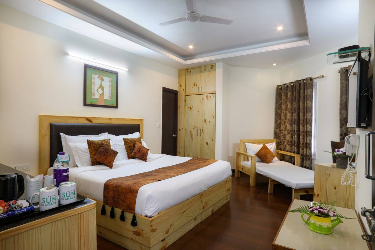 A hotel room with a large bed, a smaller bed, a desk with a chair, a wardrobe, and a television.