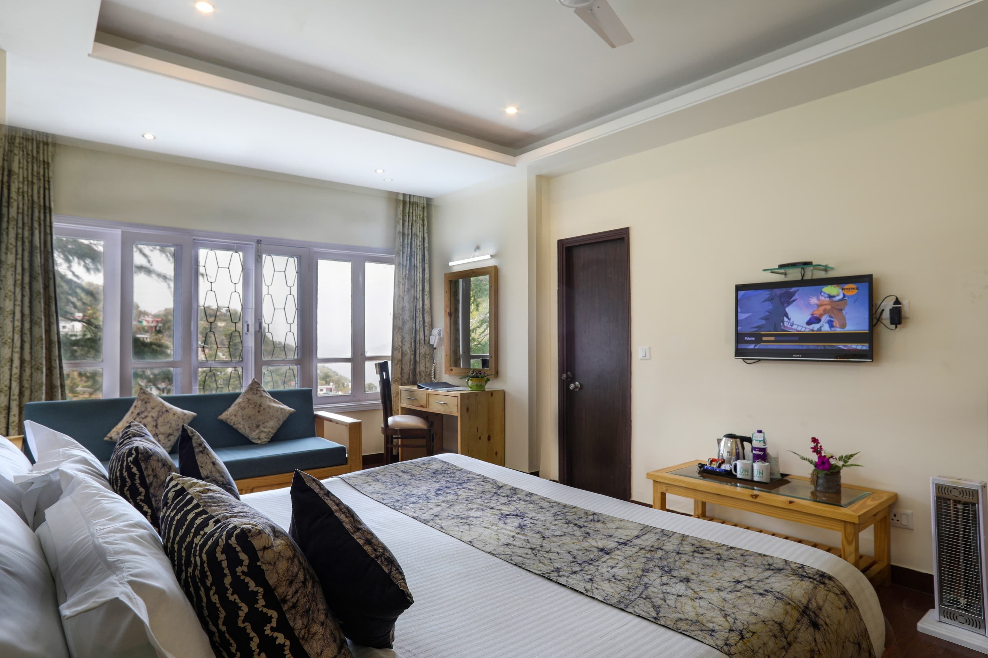 A hotel room with a large bed, a desk, a chair, a television, and a window with curtains.