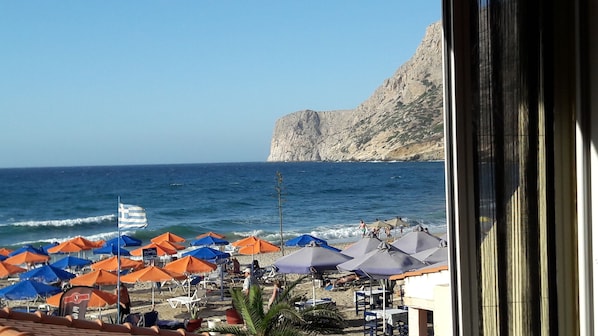 Une plage avec des parasols et des chaises, une falaise rocheuse et la mer.