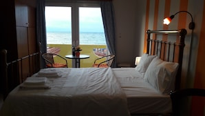 A hotel room with a bed, two chairs, a table, and a view of the sea. - Orange Fodele (Malevizi)