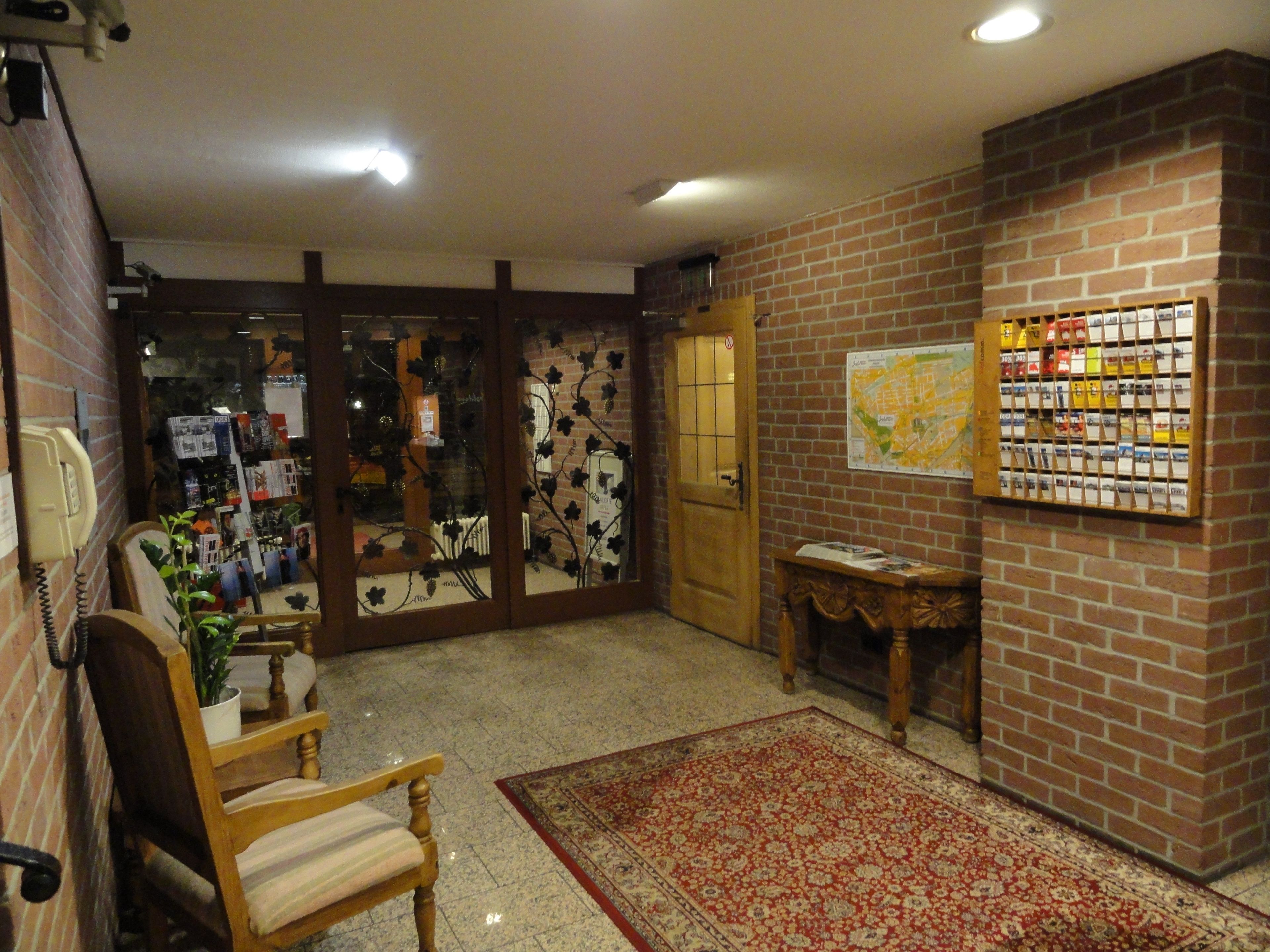 A lobby with a wooden chair, a red patterned rug, a map on the wall, and a door leading to another room.