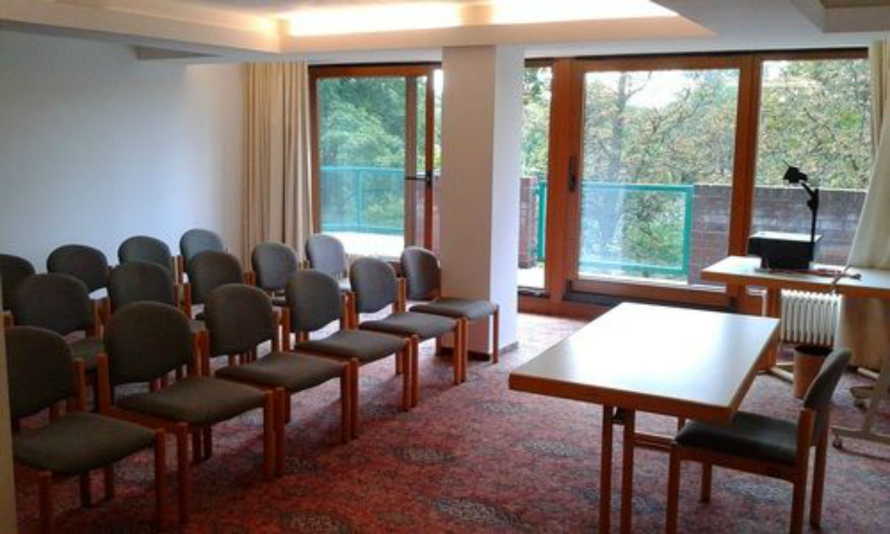 A conference room with rows of chairs, a table, and large windows with a view of trees.