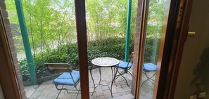 A patio with a round table and two blue cushioned chairs, surrounded by greenery and a brick wall.