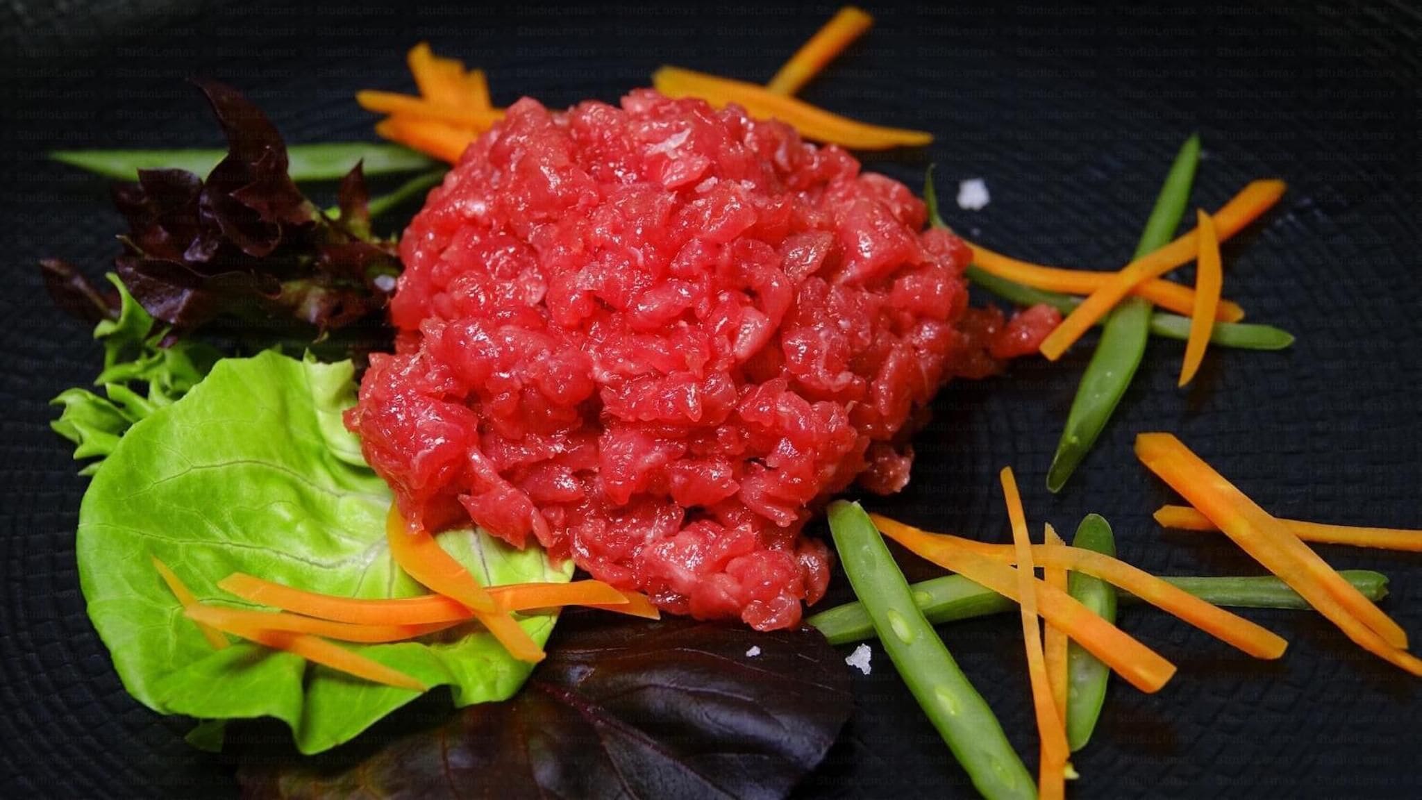 A dish with a central mound of red food, surrounded by green lettuce, orange carrot strips, and green beans on a dark plate.