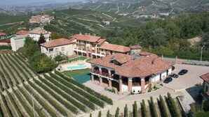 A large villa with a swimming pool, surrounded by vineyard rows, and multiple cars parked in the driveway. - Tota Virginia Antico Podere (Serralunga d'Alba)
