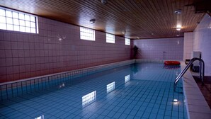 Una piscina interior con paredes y techo azulejados, un borde de piscina transparente y un flotador rojo.