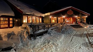 A snow-covered building with a wooden facade and a red roof, featuring large windows and a wooden staircase leading to the entrance. - Skjerdingen Høyfjellshotel (Ringebu)