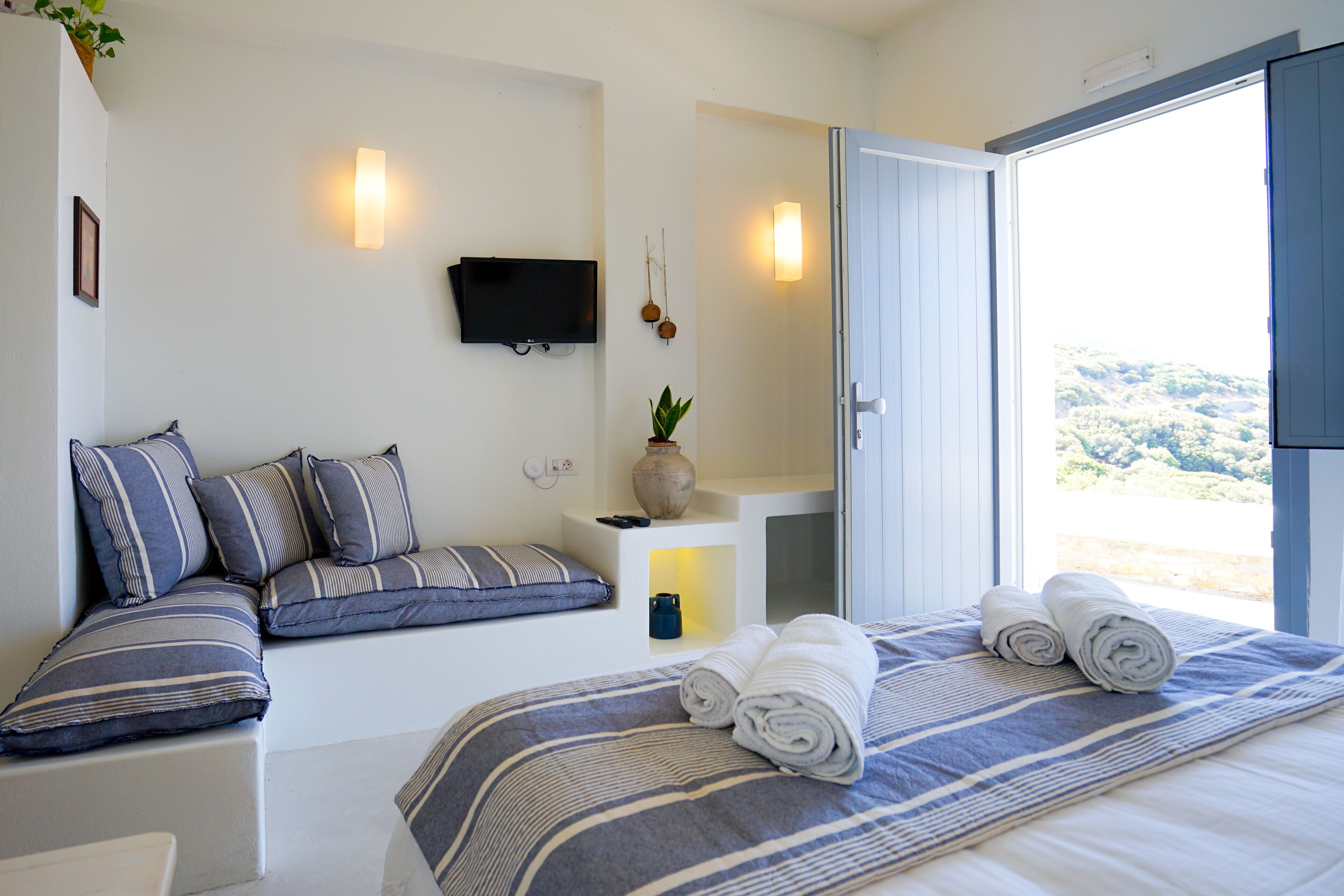 Een slaapkamer met een bed, kussens, een televisie, een plant en uitzicht op het landschap.