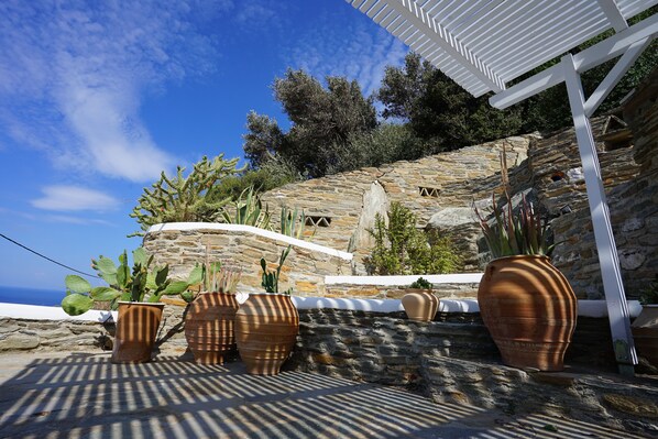 A stone wall with potted plants and a white pergola. - Villa Alisachni (Andros)