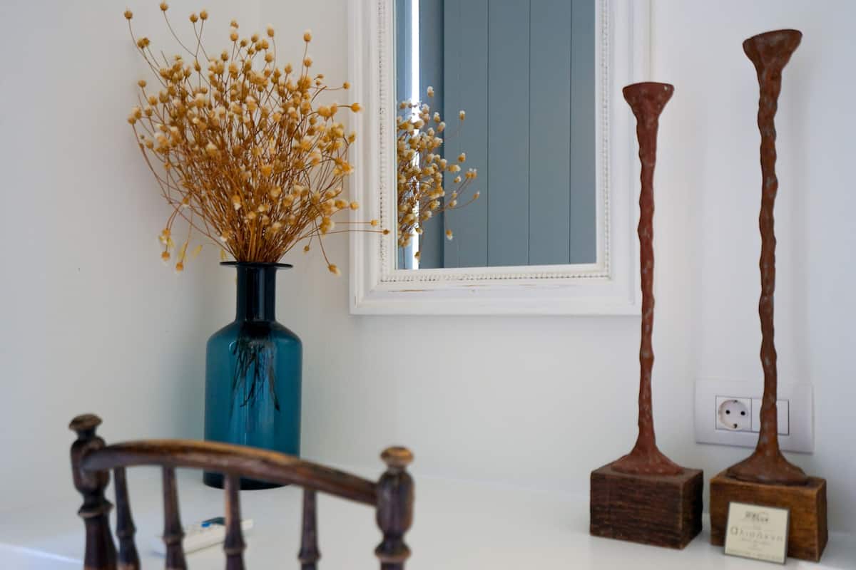A vase with dried flowers, a mirror, and two wooden sculptures on a table.
