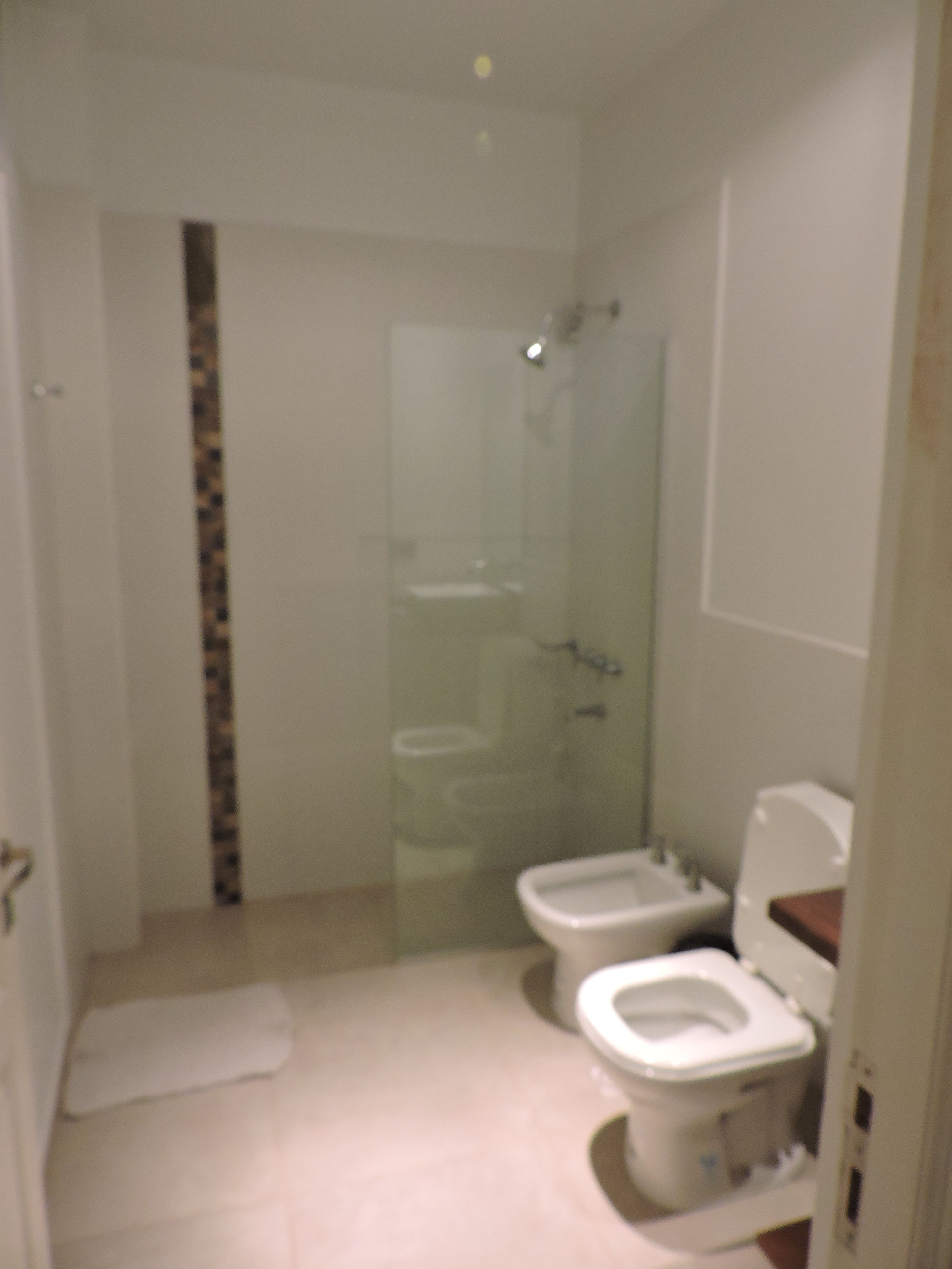 Un baño con cabina de ducha de vidrio, dos inodoros y un lavamanos.