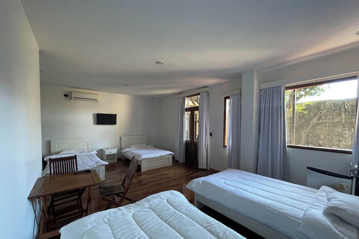 A room with two single beds, a wooden desk, a chair, a television mounted on the wall, and a window with curtains.