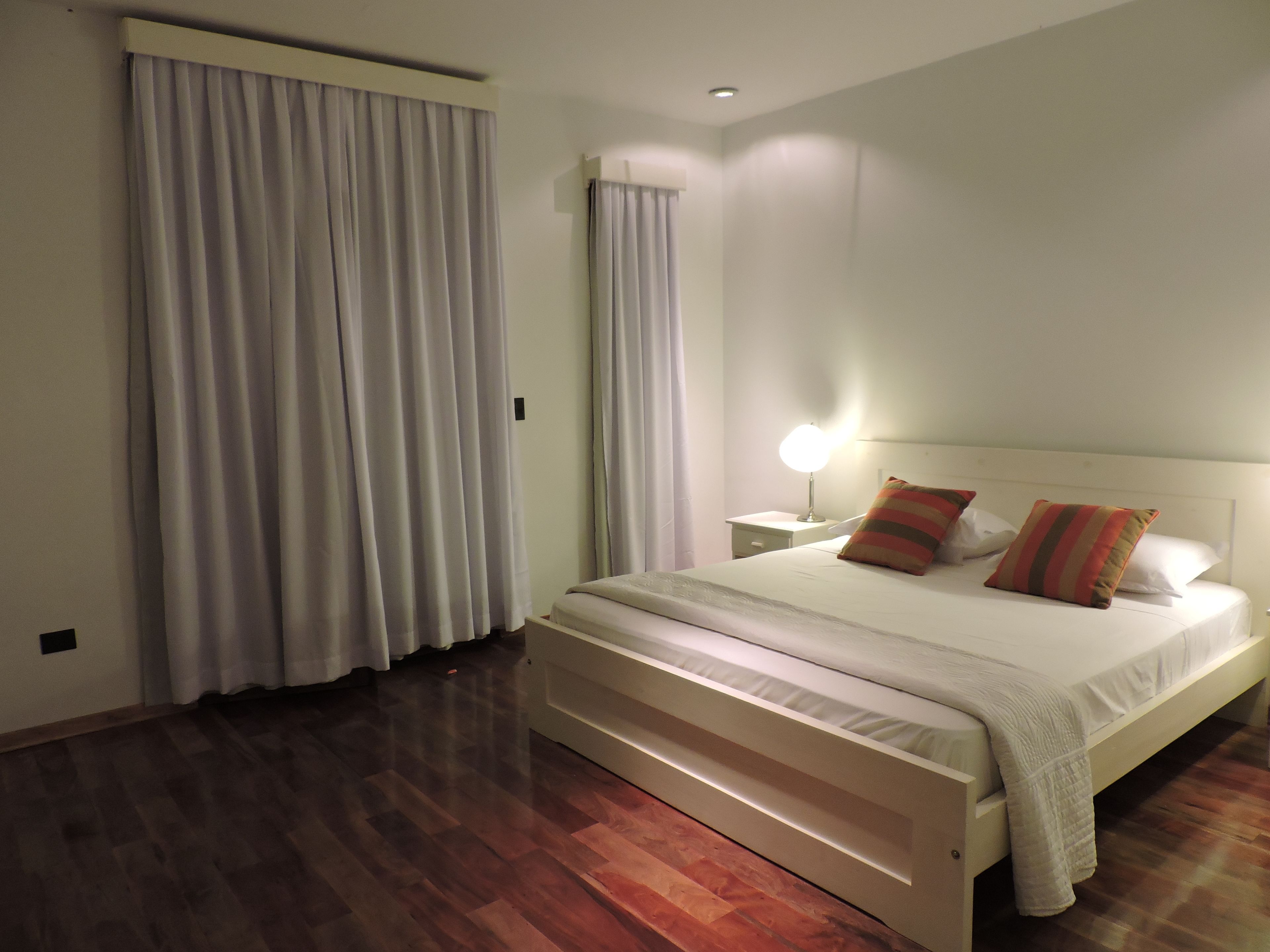A hotel room with a large bed, a bedside table with a lamp, and a window with curtains.