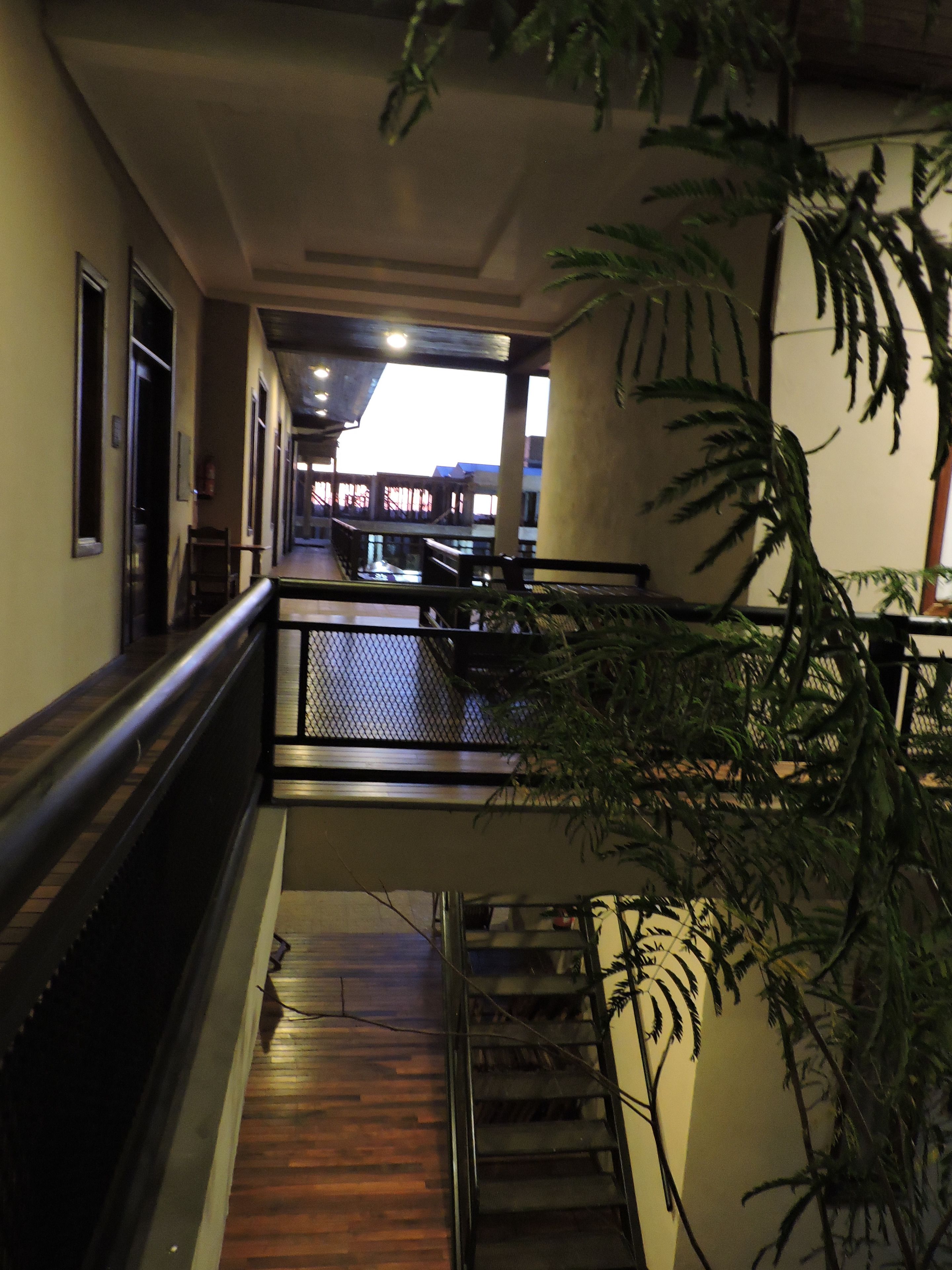 A corridor with a wooden floor, metal railing, and a staircase leading to an upper level.
