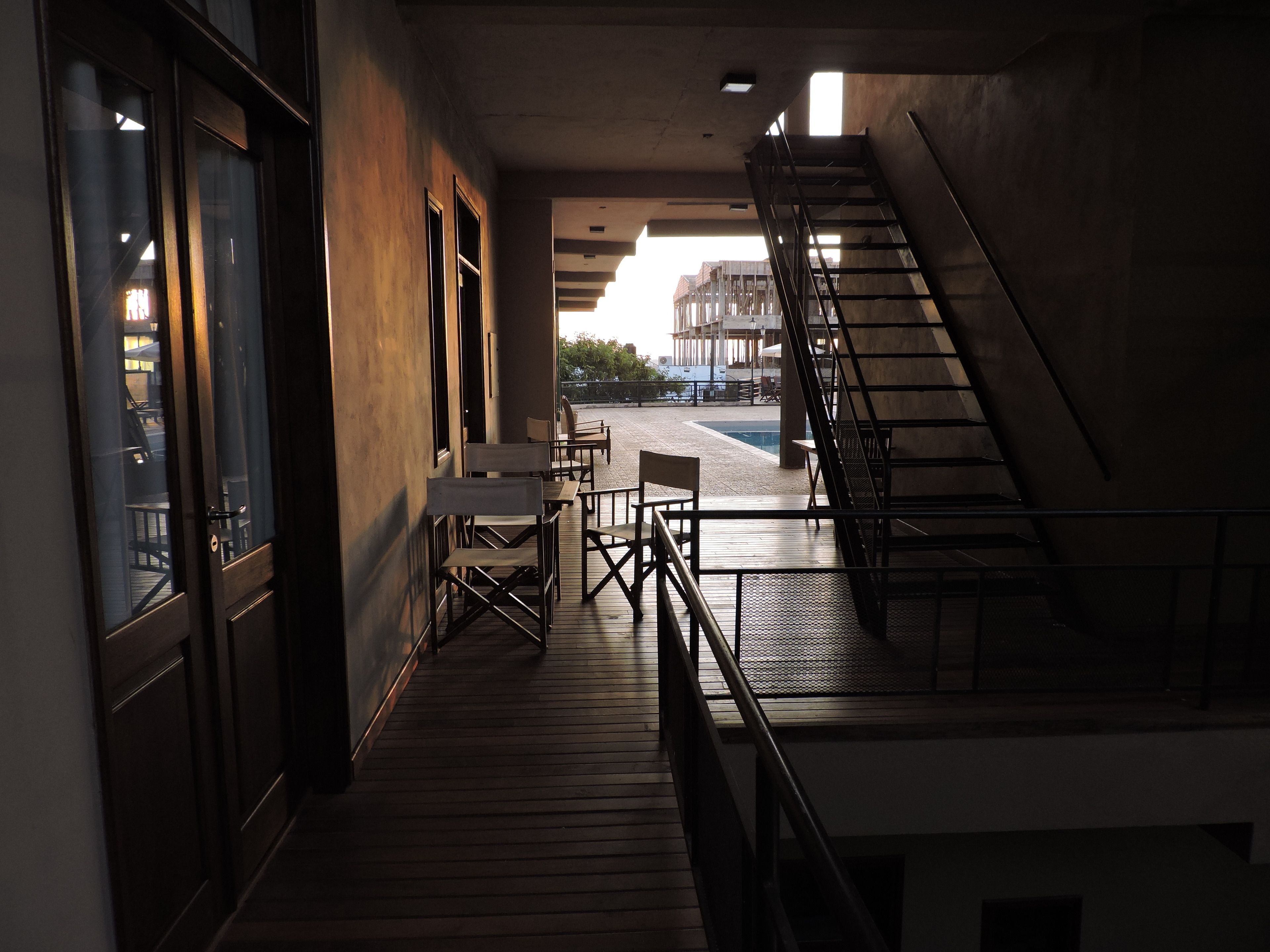 A corridor with a wooden floor leading to a staircase and a seating area with tables and chairs.