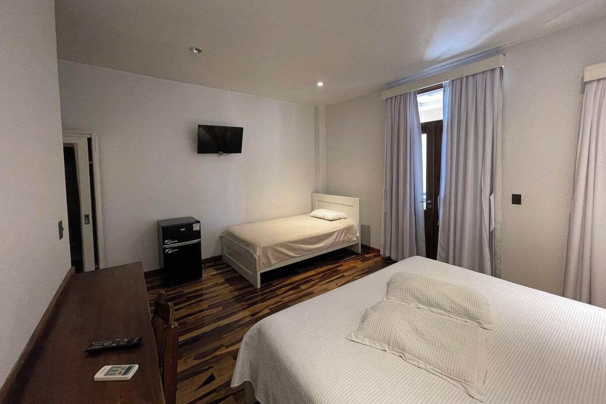 A hotel room with a bed, a desk, a TV, and a window with curtains.