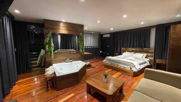 Ein modernes Hotelzimmer mit einem großen Bett, einer separaten Sitzecke mit einer Couch und einem kleinen Tisch, Holzboden und einem großen Fenster.