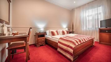 Een hotelkamer met een groot bed, een bureau met stoel, een televisie en een raam met dunne gordijnen.