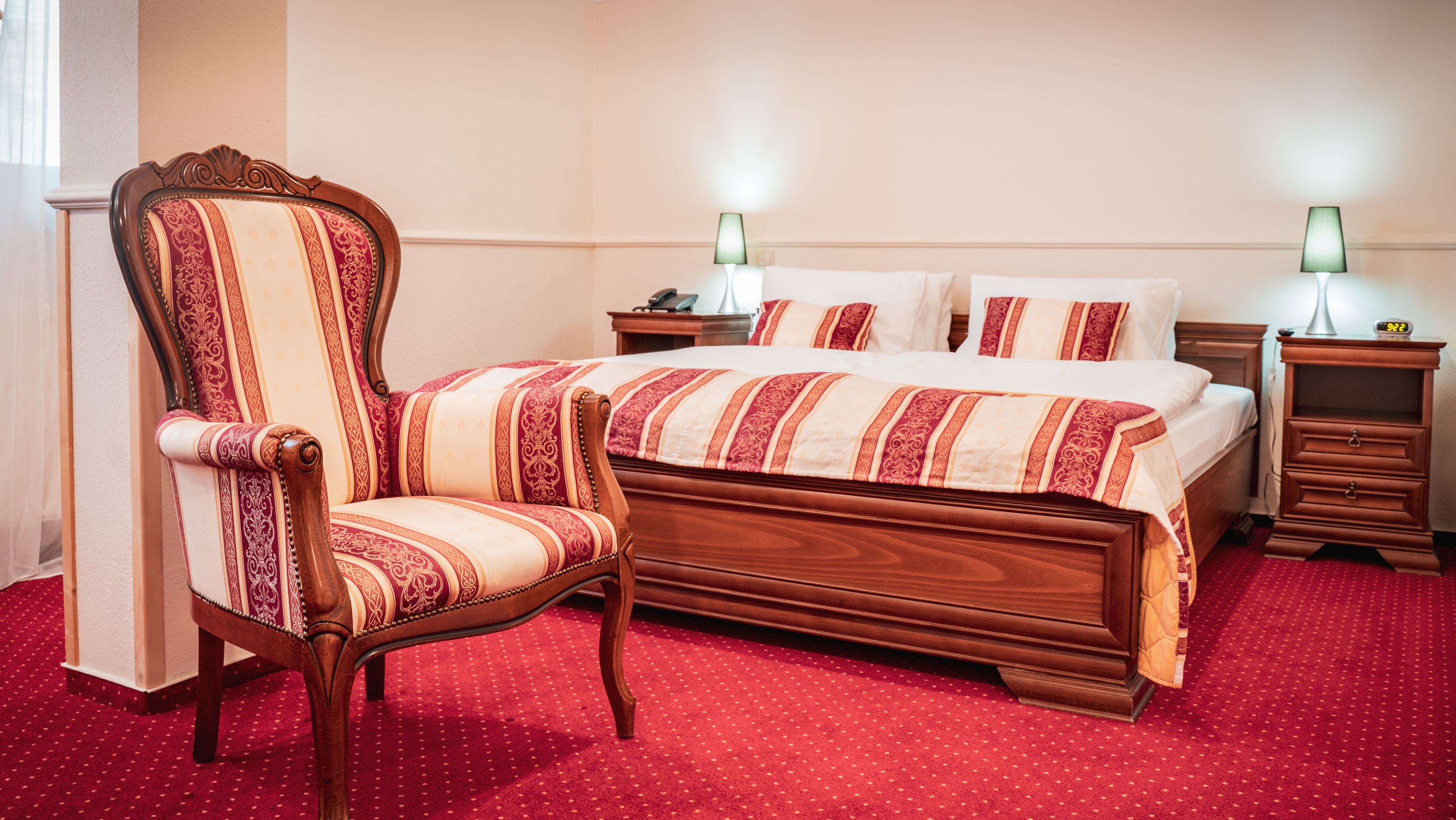 Un dormitorio con una cama de madera, una silla a juego, dos mesitas de noche y una alfombra roja.