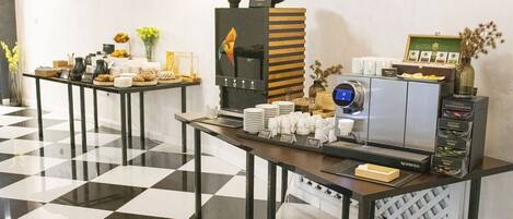 A breakfast buffet area with a coffee machine, plates, cups, and various food items.