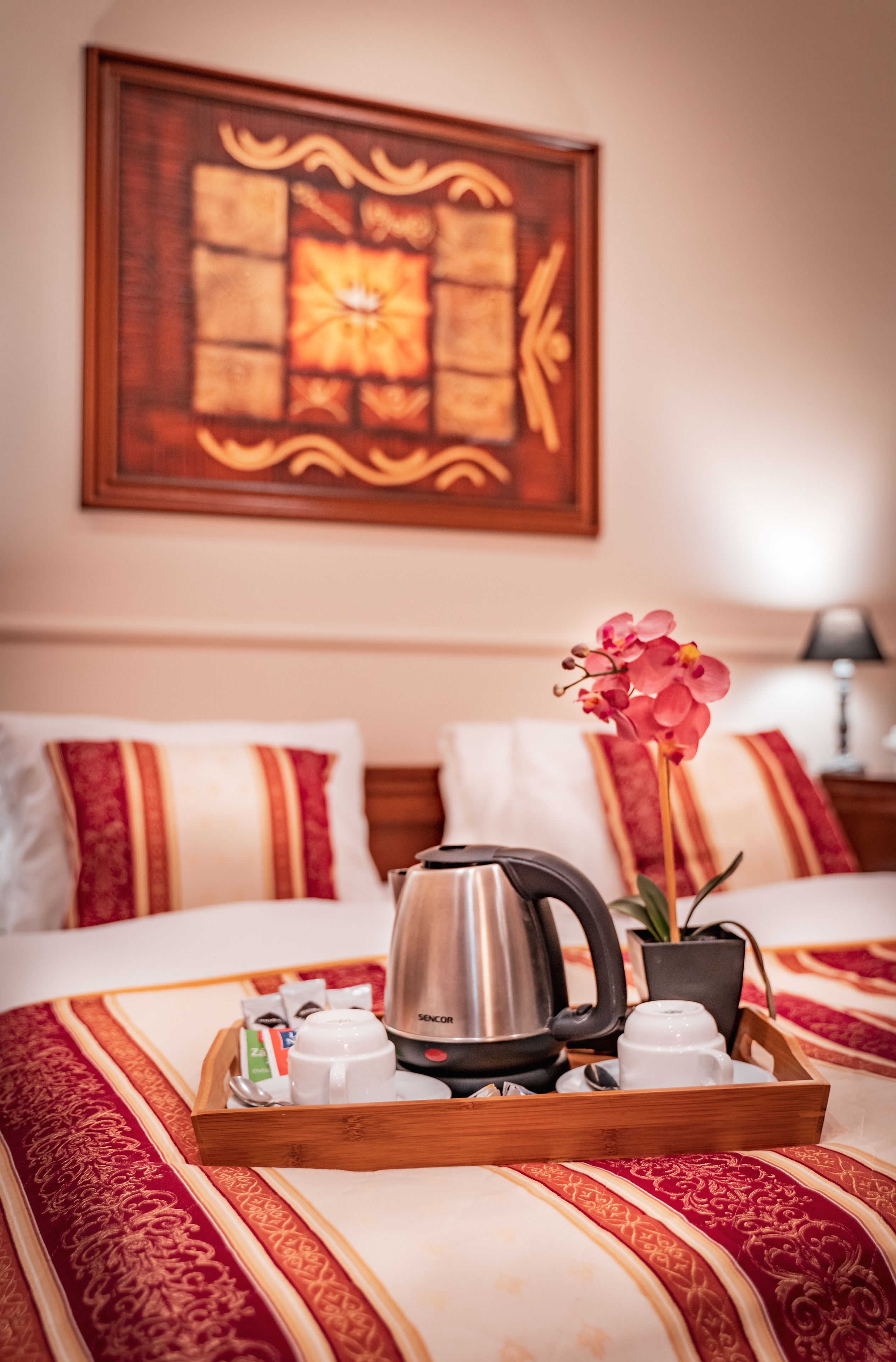 Une chambre d’hôtel avec un lit, un plateau avec du café et du thé, une fleur et un tableau au mur.