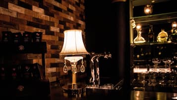 Zona de bar con pared de ladrillo de madera, una lámpara encendida y una estantería con botellas y vasos.