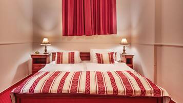 Ein Hotelzimmer mit einem großen Bett, zwei Nachttischen mit Lampen, einem roten Vorhang und einem roten Teppich.