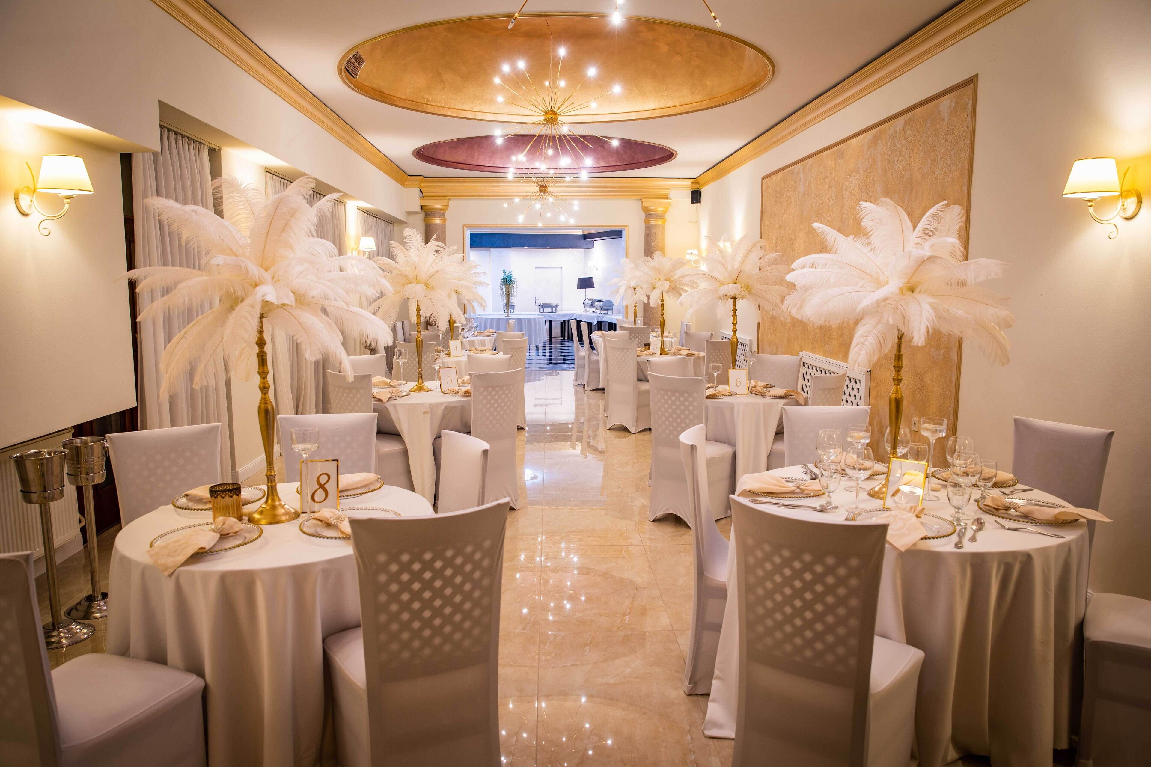 A formal dining room with round tables, white chairs, and large white feather arrangements.
