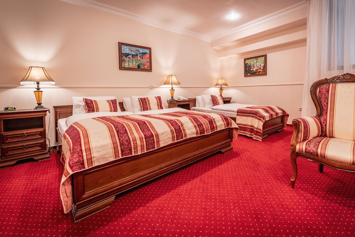 A hotel room with two beds, a wooden nightstand, a chair, and two paintings on the walls.