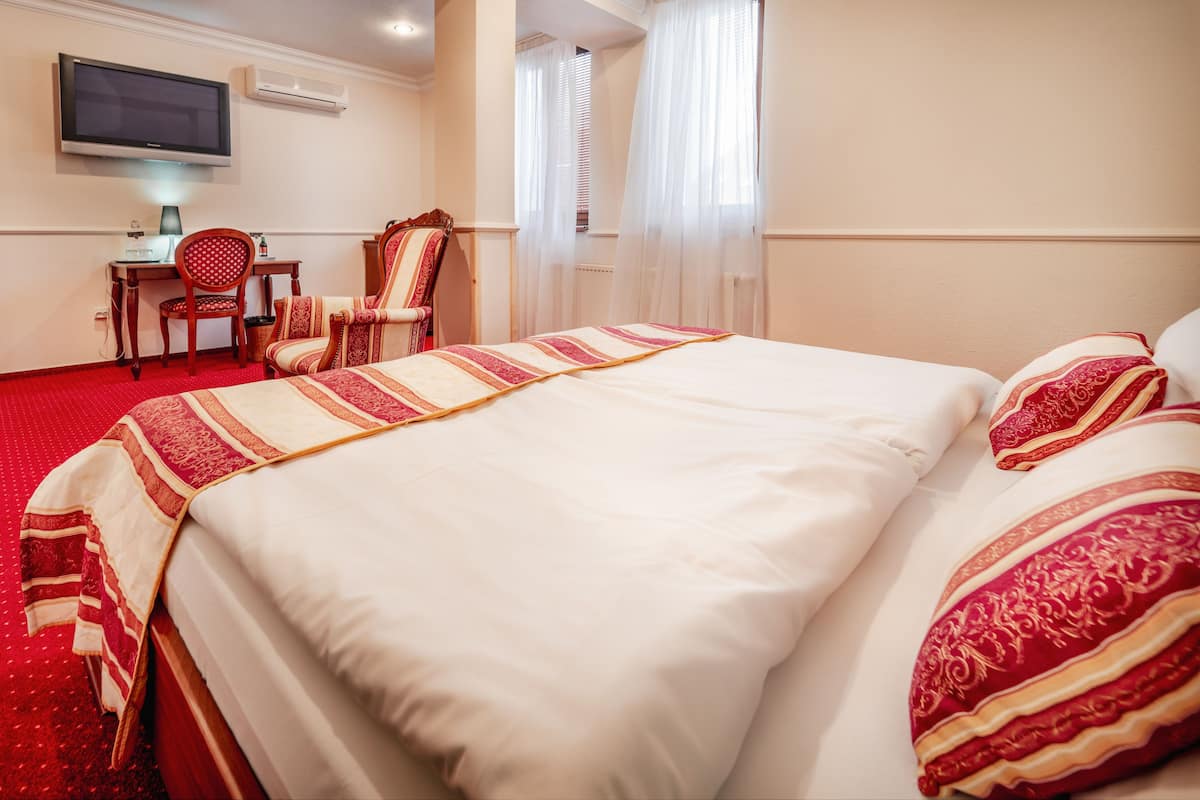 A hotel room with a large bed, a desk with a chair, a television, and a window with curtains.