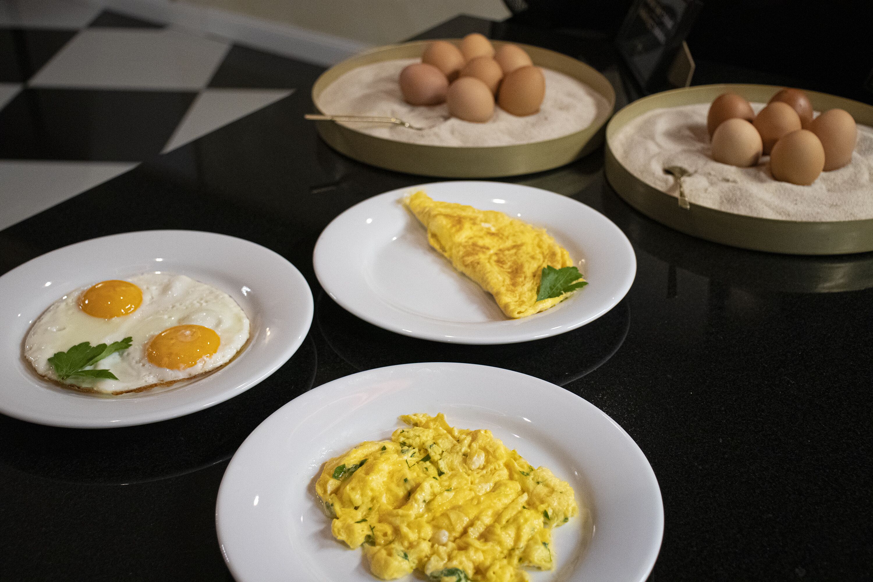 Una mesa con tres platos de comida: dos huevos fritos, una tortilla y revuelto de huevo.