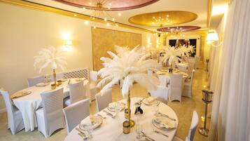 Un comedor formal con mesas redondas, sillas blancas y centros de mesa con plumas.