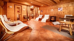 A wooden cabin interior with a fireplace, reclining chairs, a small table, and a clock on the wall. - Hotel Capital (Nitra)