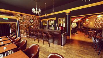 A restaurant interior with wooden tables and chairs, a bar area, and a chandelier.