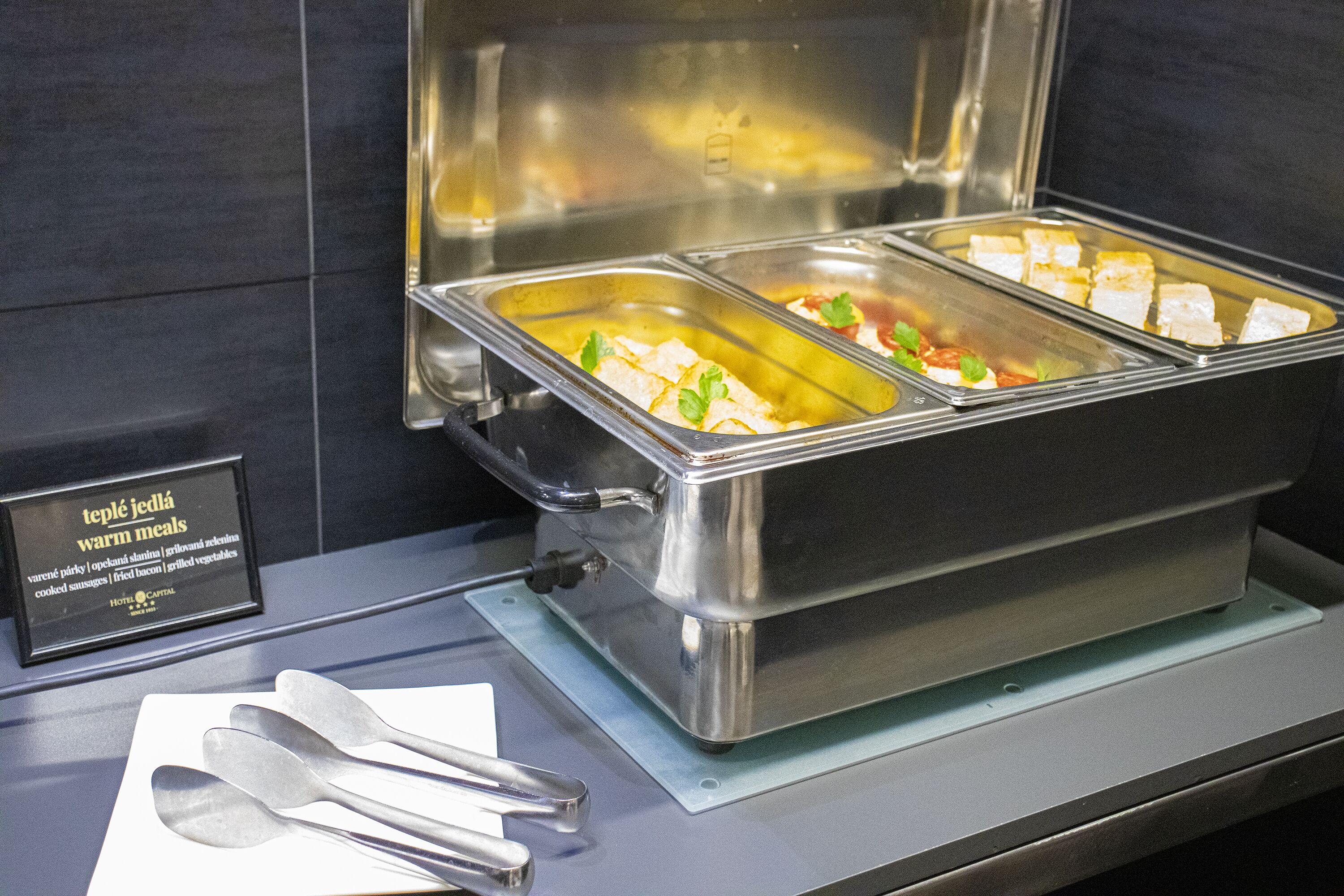A buffet setup with labeled containers for various warm meals, including a sign indicating the type of meals available.