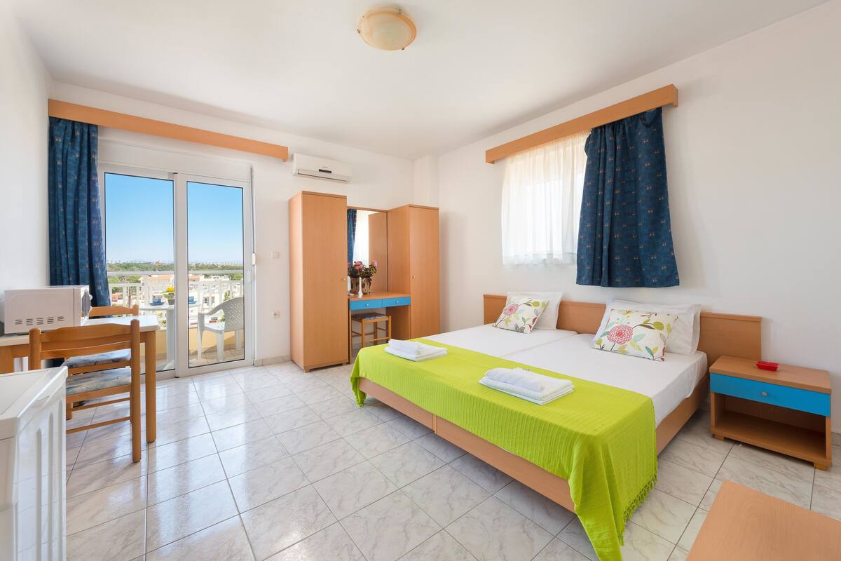 Une chambre d’hôtel avec un lit, un bureau, une chaise, une table de chevet et une vue sur la ville par la fenêtre.