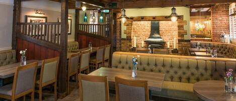 A restaurant with wooden tables and booths, a brick wall, and a fireplace.