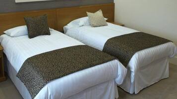 Habitación de hotel con dos camas, cada una con ropa blanca y mantas marrones. En la pared, encima de las camas, hay un cuadro.