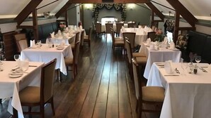 Un comedor interior con vigas de madera, manteles blancos y sillas.